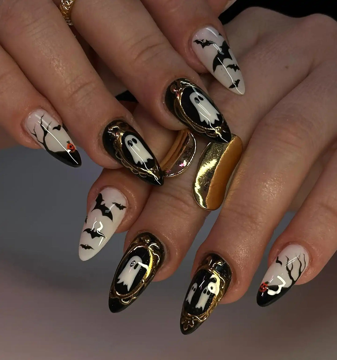 Hand with long stiletto press-on nails featuring Halloween ghost and bat nail art designs.