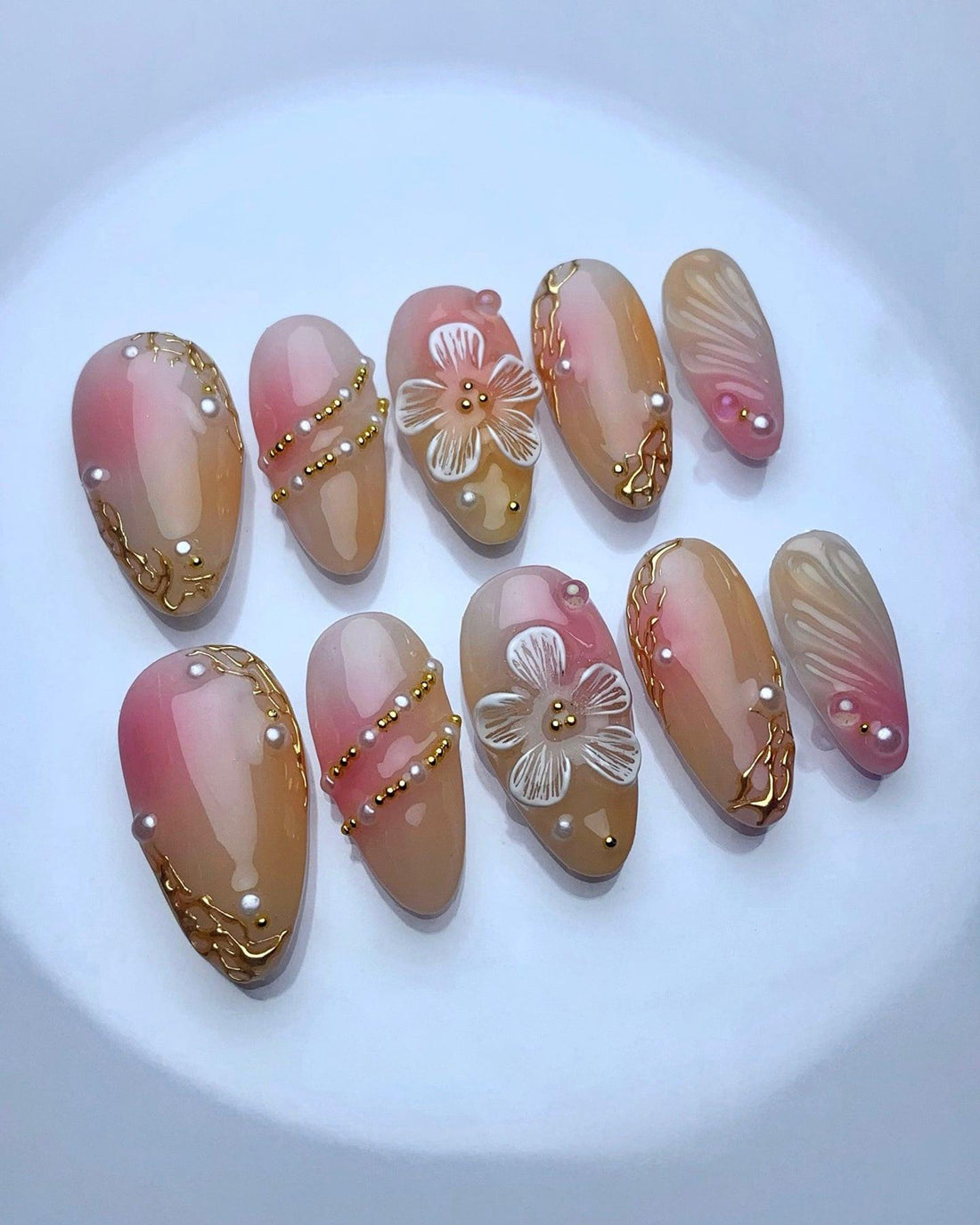 Handmade press-on nails with pink and nude ombre, gold accents, pearls, and floral designs.