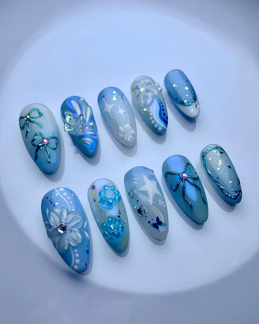 Blue and white handmade press-on nails with floral, bow, star, and butterfly designs