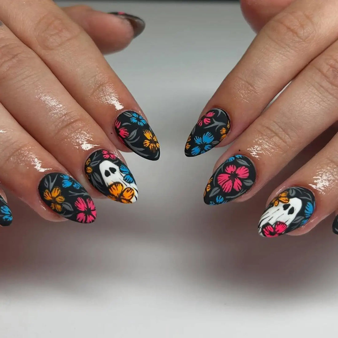 Handmade press-on nails with black base, colorful floral patterns, and skull accents.