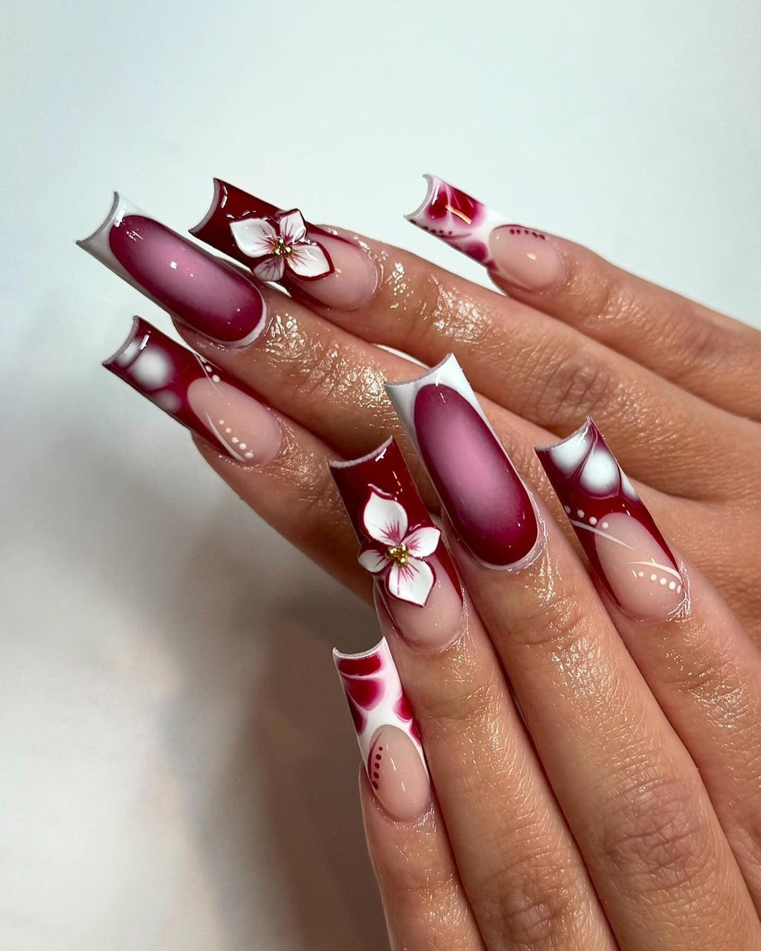 Hand with long, burgundy and white floral press-on nails, glossy finish, custom nail art