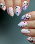 Hand with pastel Halloween press-on nails featuring pumpkins, ghosts, boo text, and leafy designs.