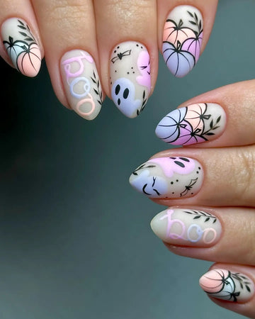 Hand with pastel Halloween press-on nails featuring pumpkins, ghosts, boo text, and leafy designs.