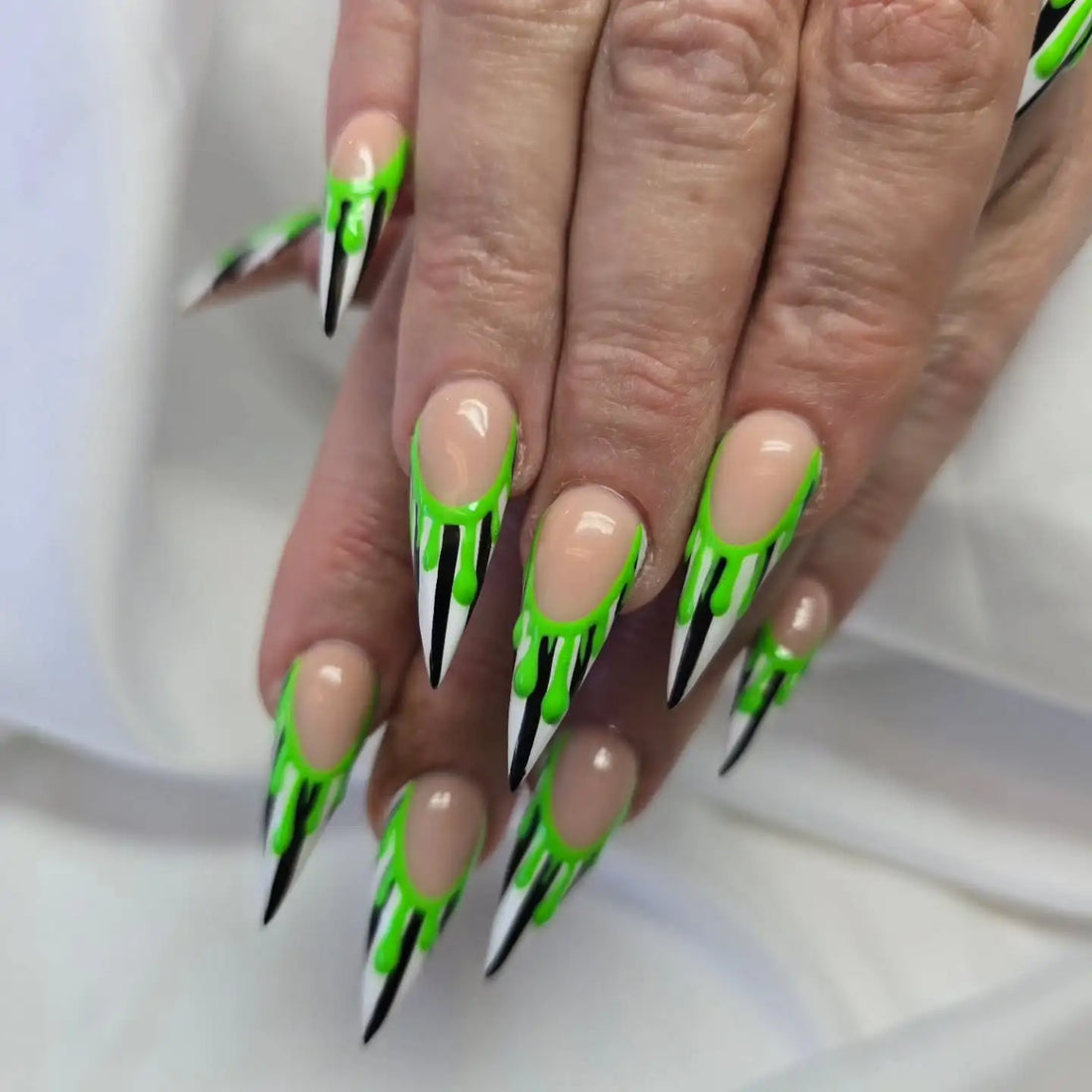 Stiletto press-on nails with neon green drip design and black and white tips on hands
