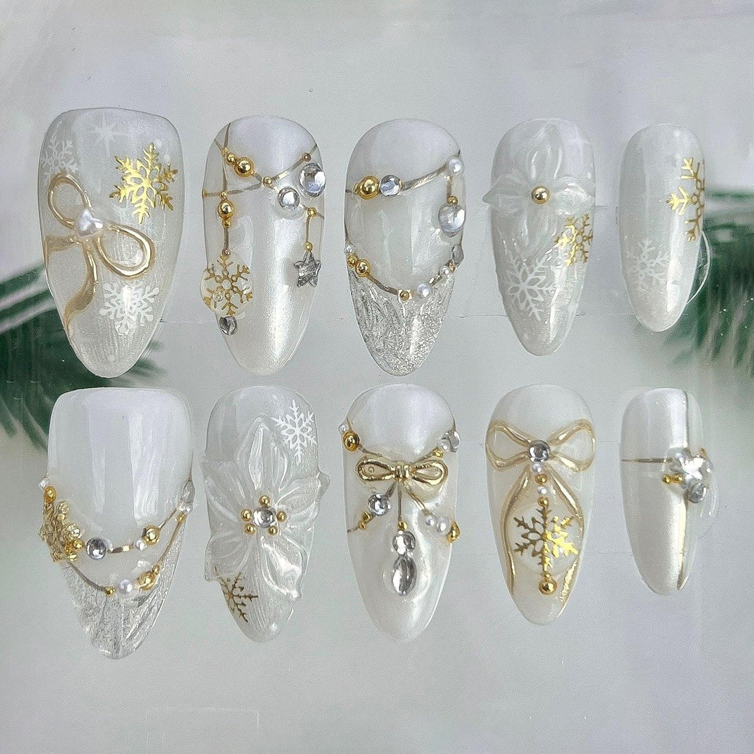 White and gold winter-themed press-on nails with snowflake, bow, and pearl designs