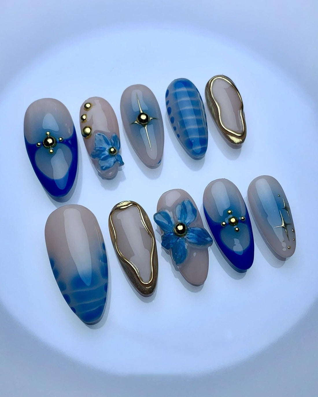Handmade blue press-on nails with gold accents and floral 3D designs