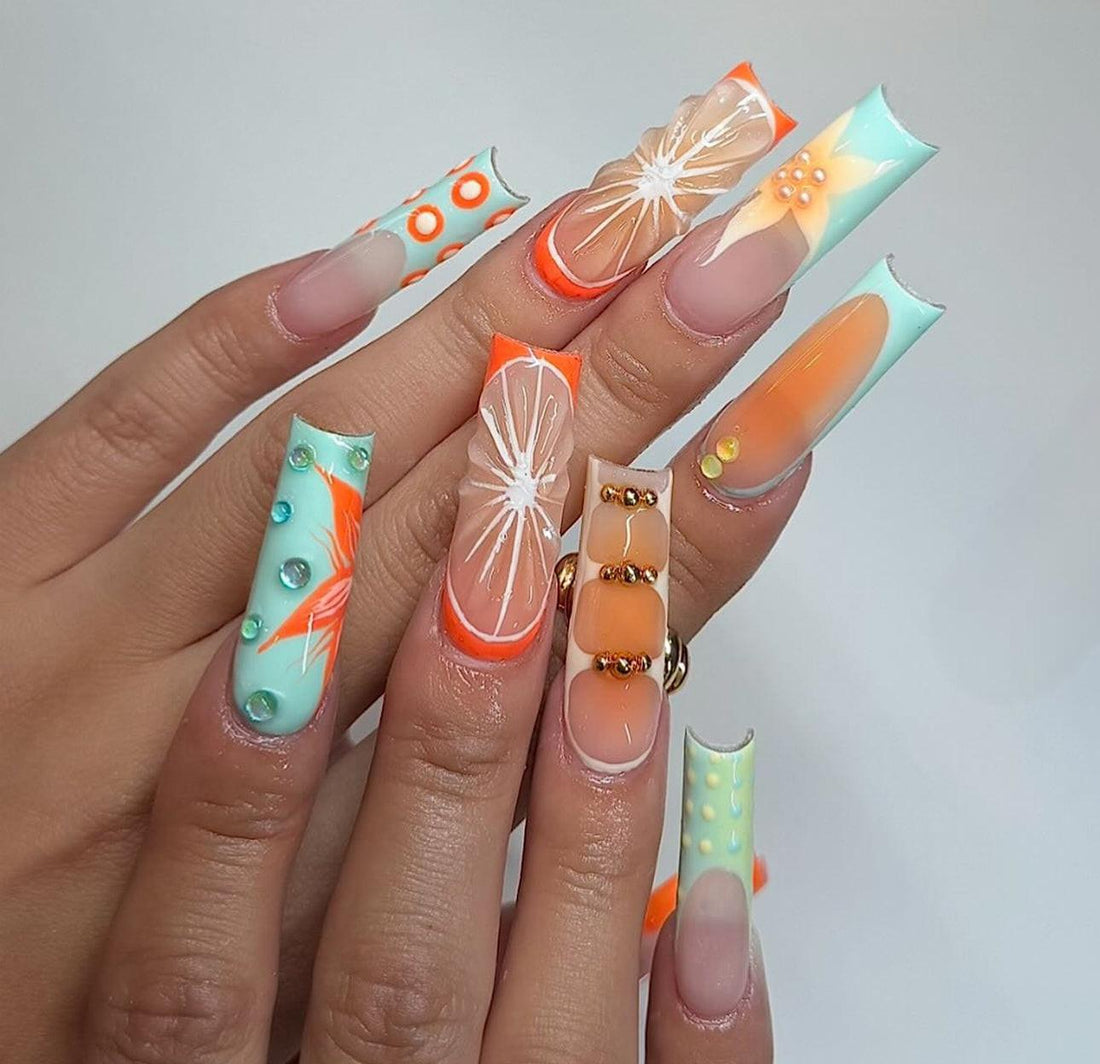 Hand with long press-on nails in orange, turquoise, and nude, featuring 3D floral and geometric designs