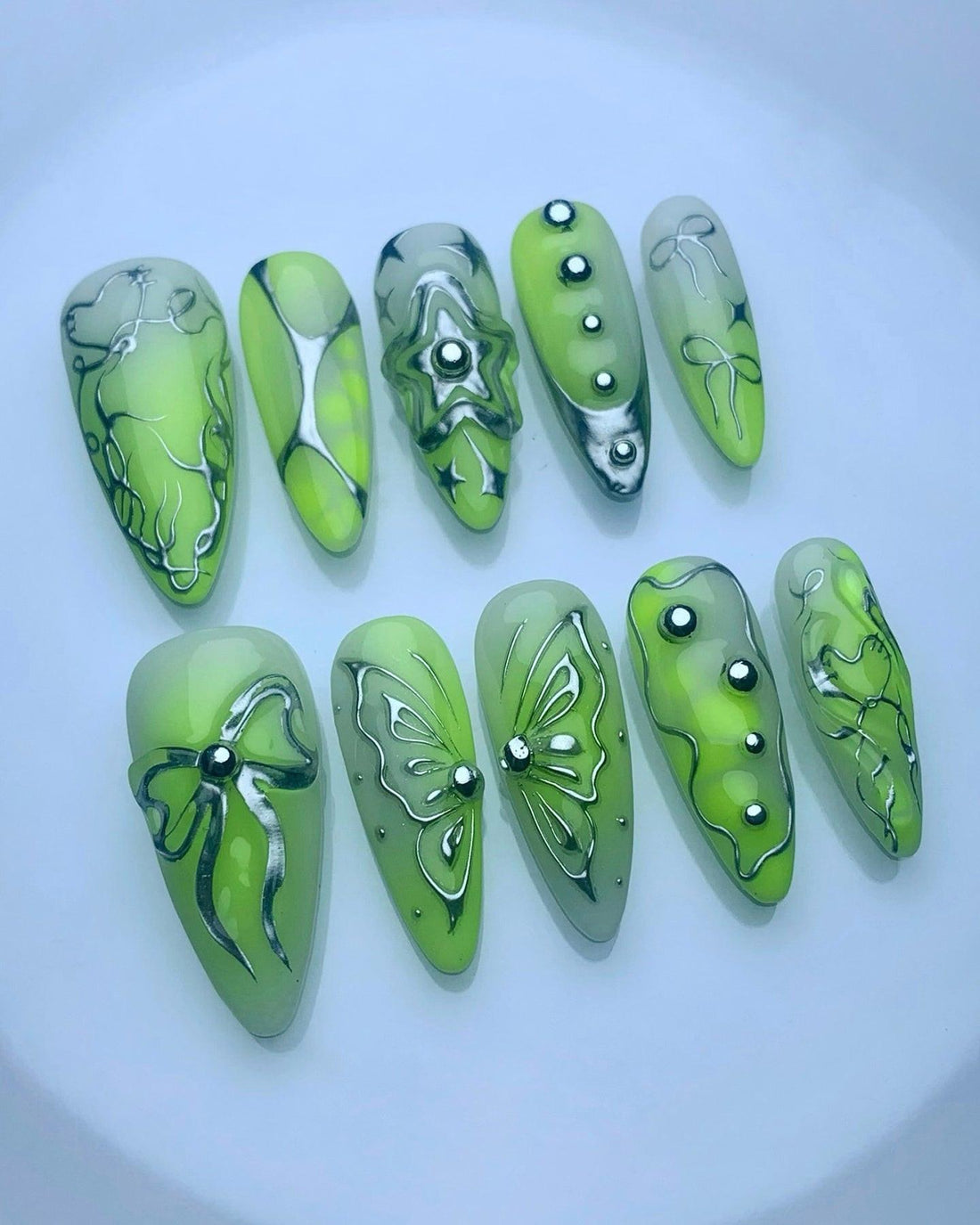 Handmade green press-on nails with metallic butterfly, bow, and star designs, gemstone accents