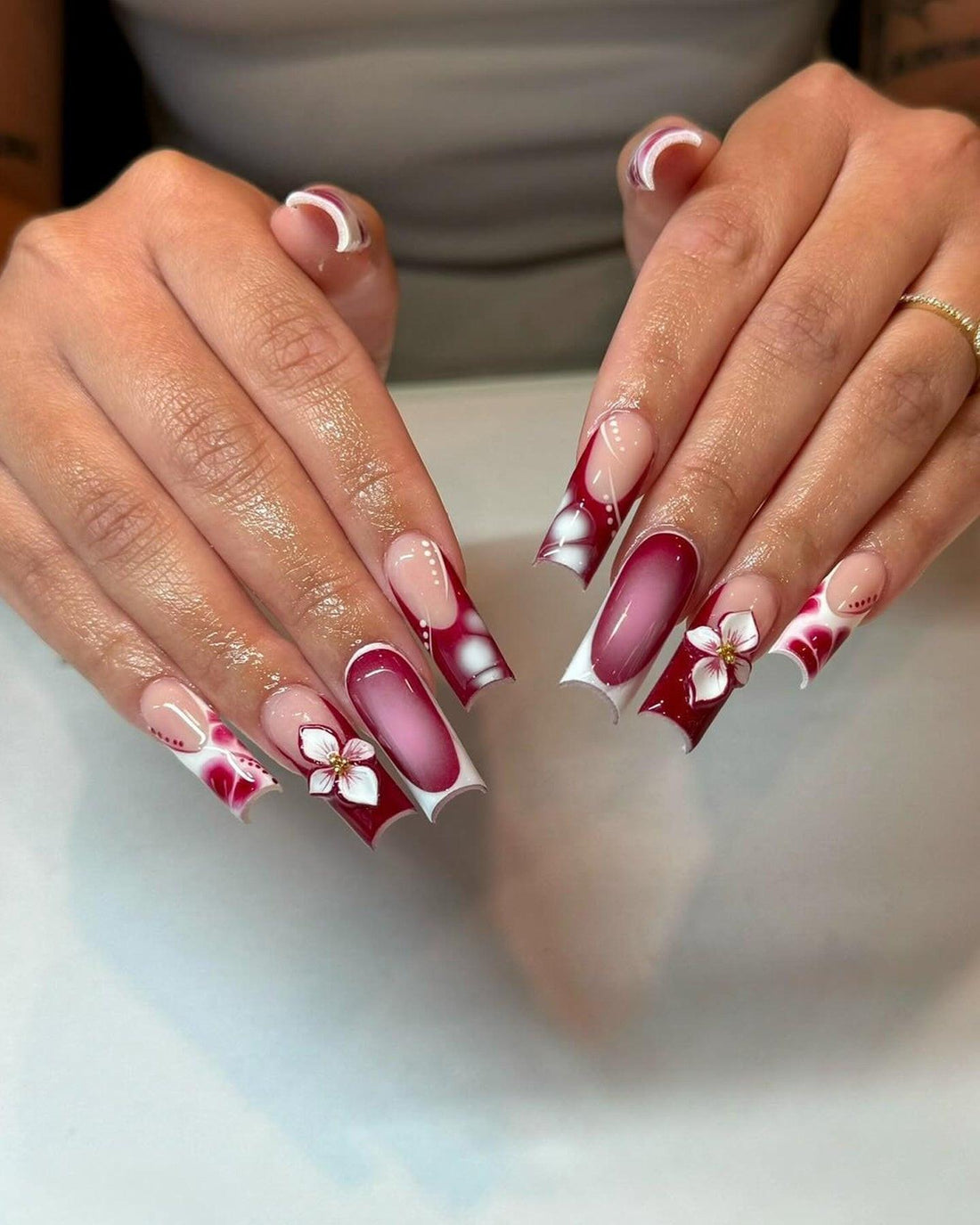 Hand with long, burgundy and white floral press-on nails, glossy finish, custom nail art