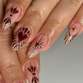 Hand with custom press-on nails featuring gold and red heart and star designs on nude base