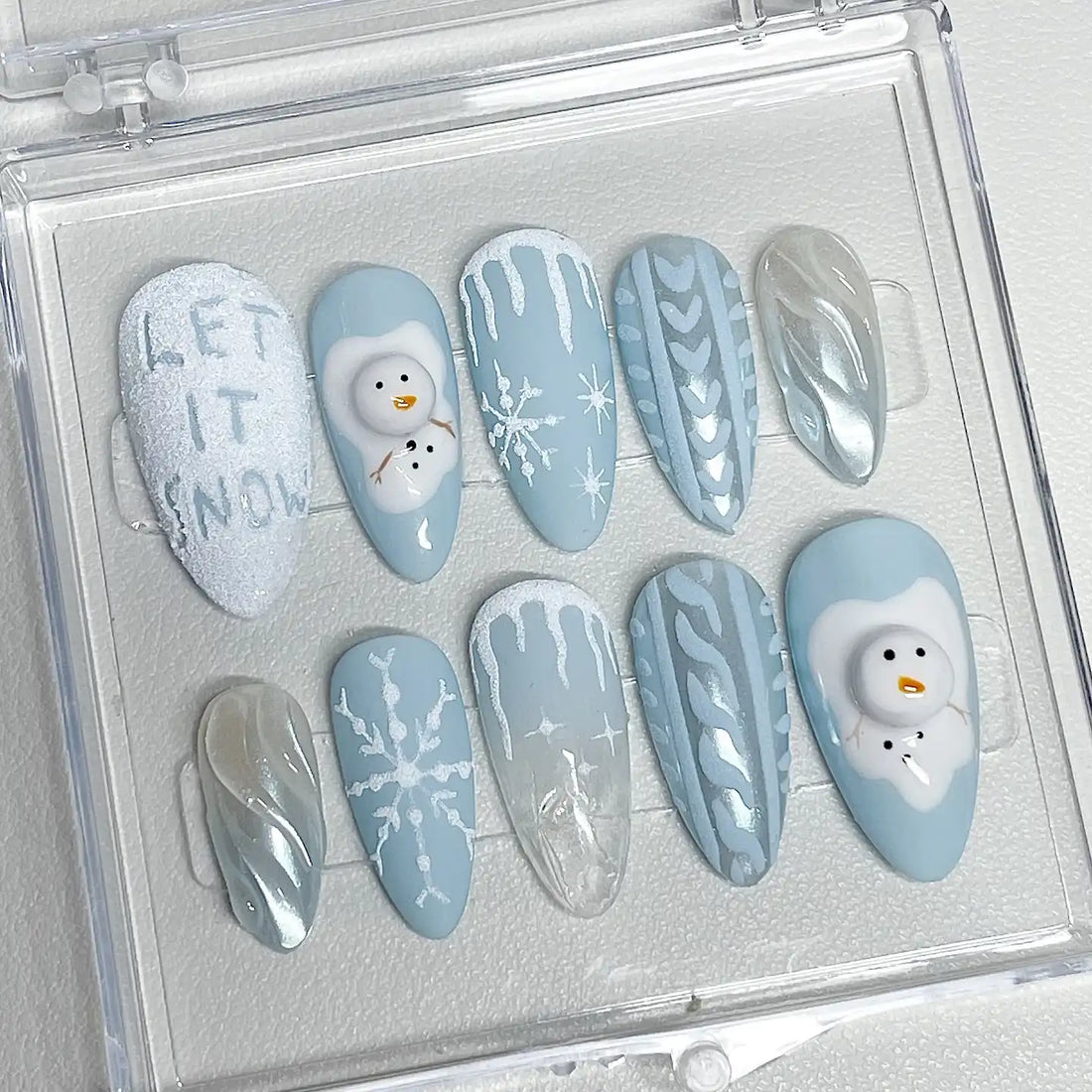 Handmade blue winter press-on nails with snowman, snowflake, icicle and sweater designs.