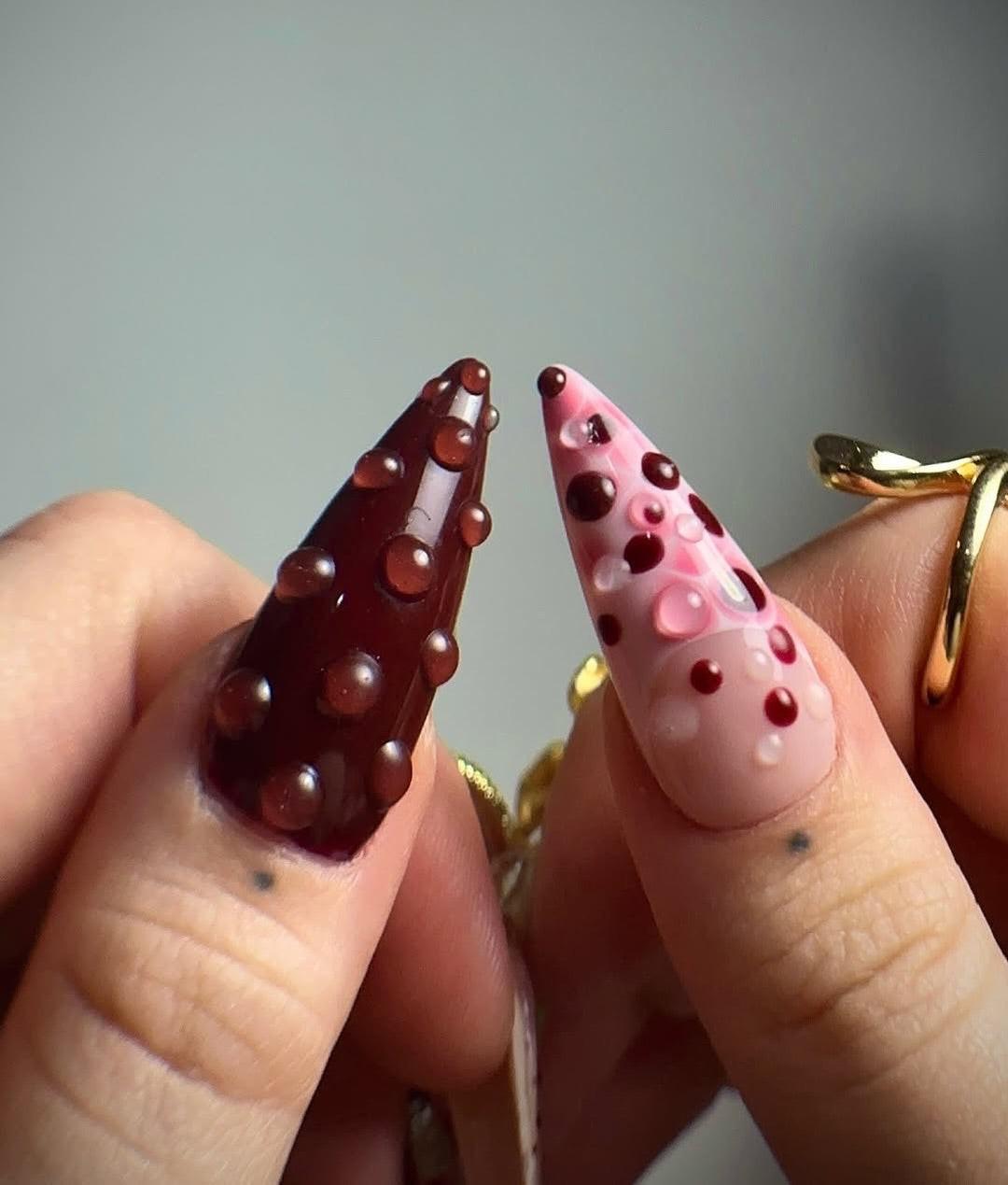 Hand with long stiletto press-on nails featuring 3D floral designs, rhinestones, and gold rings