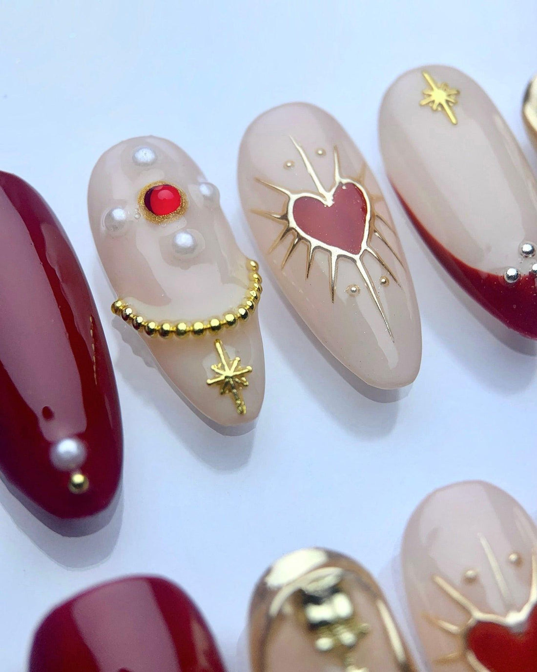 Handmade press-on nails with red, gold, and nude designs, heart and rose accents, reusable