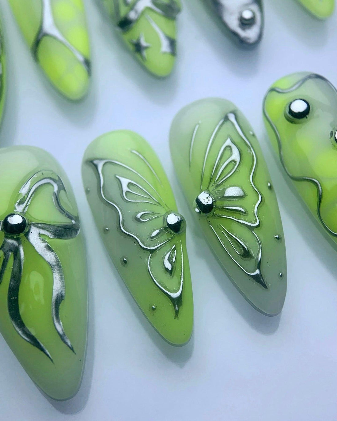 Handmade green press-on nails with metallic butterfly, bow, and star designs, gemstone accents