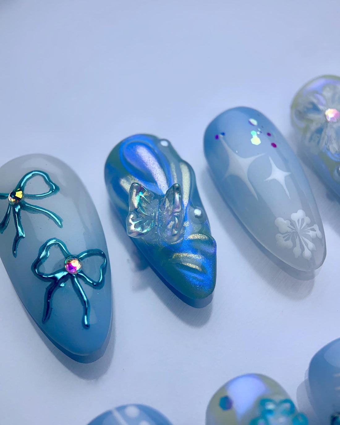 Blue and white handmade press-on nails with floral, bow, star, and butterfly designs