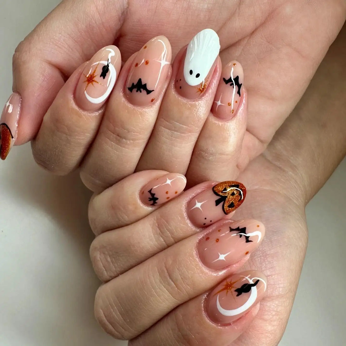 Halloween press-on nails with bats, ghost, pumpkin, and glittery accents on nude base