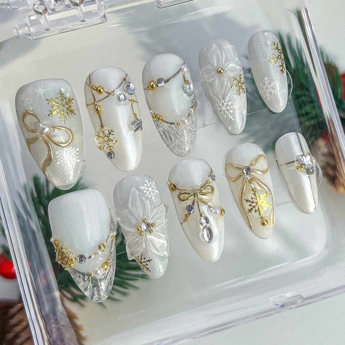 White and gold winter-themed press-on nails with snowflake, bow, and pearl designs