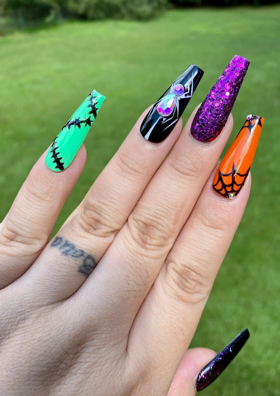 Hand with long press-on nails featuring Halloween designs, glitter, spider web, and rhinestones.