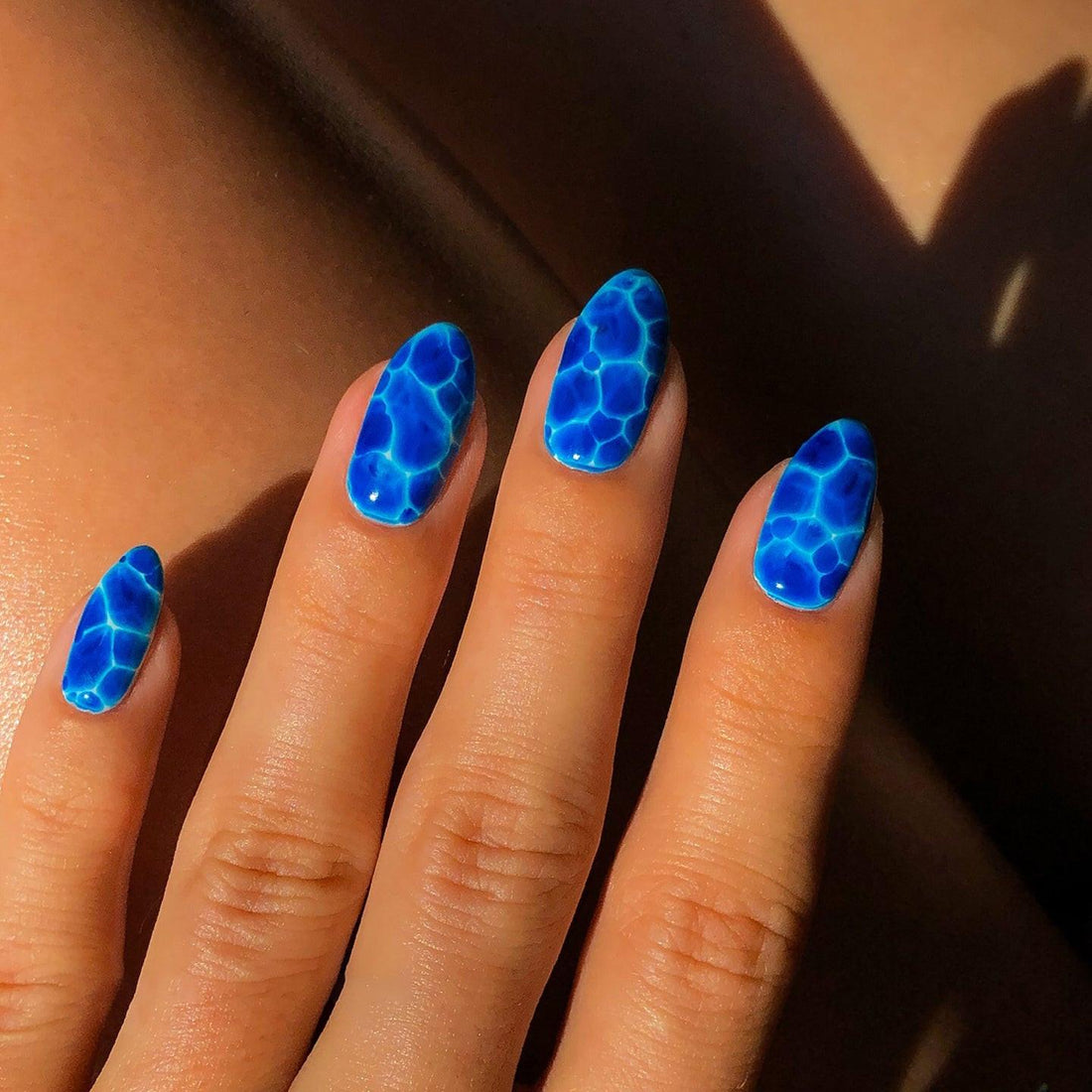 Hand with custom blue press-on nails featuring a water ripple design in sunlight