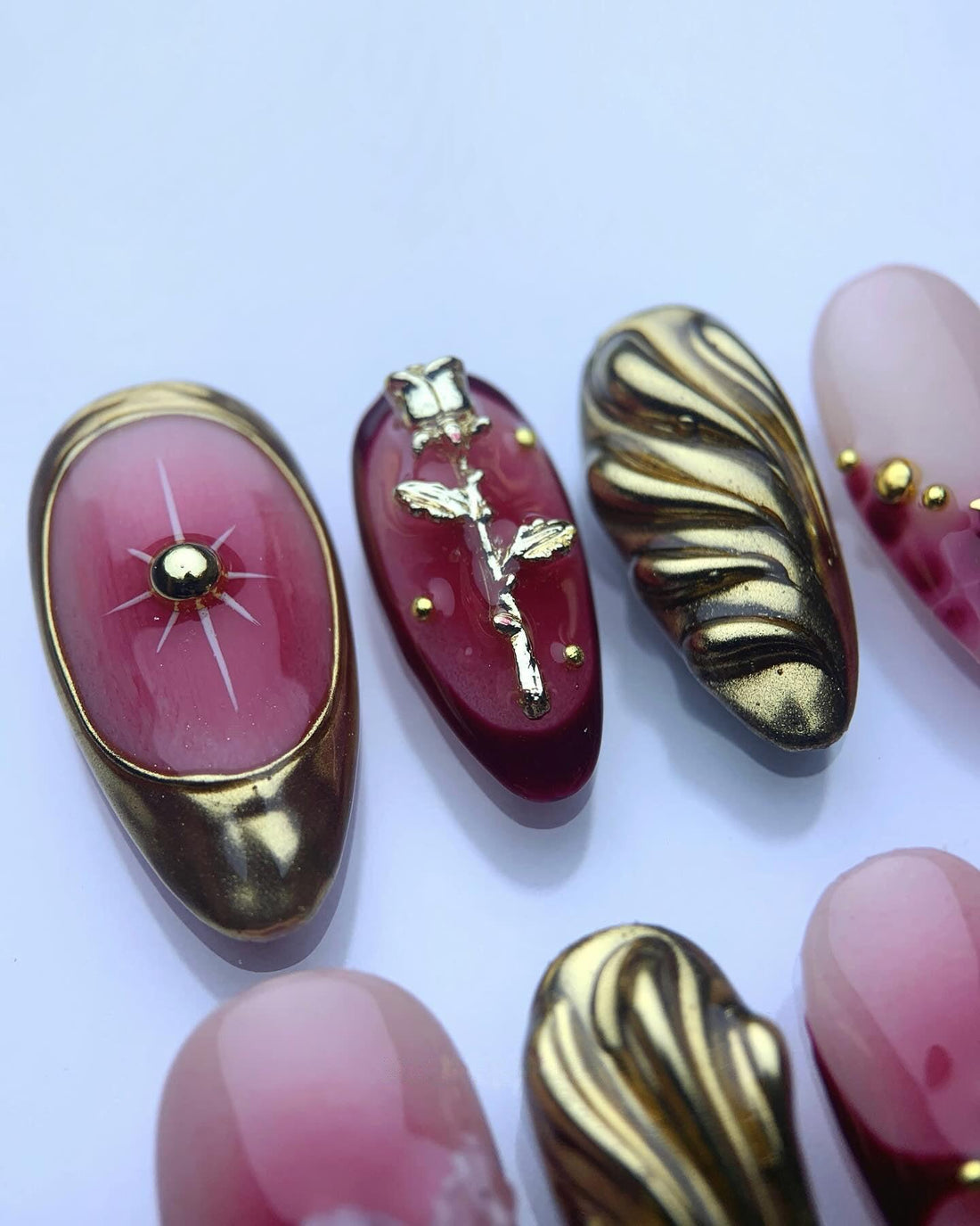 Handmade press-on nails in burgundy and gold with floral and metallic designs