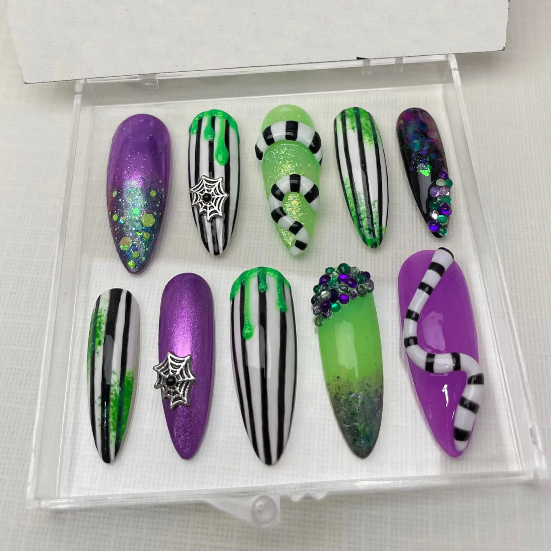 Halloween press-on nails with Beetlejuice-inspired green, purple, and black designs, glitter, spider webs, and gemstone accents.