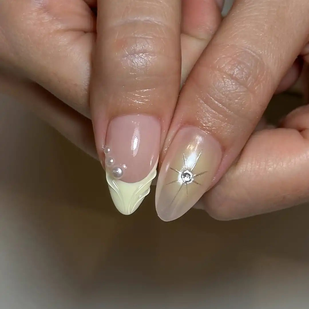 Hand with light yellow French tip press-on nails, 3D floral designs and pearl accents