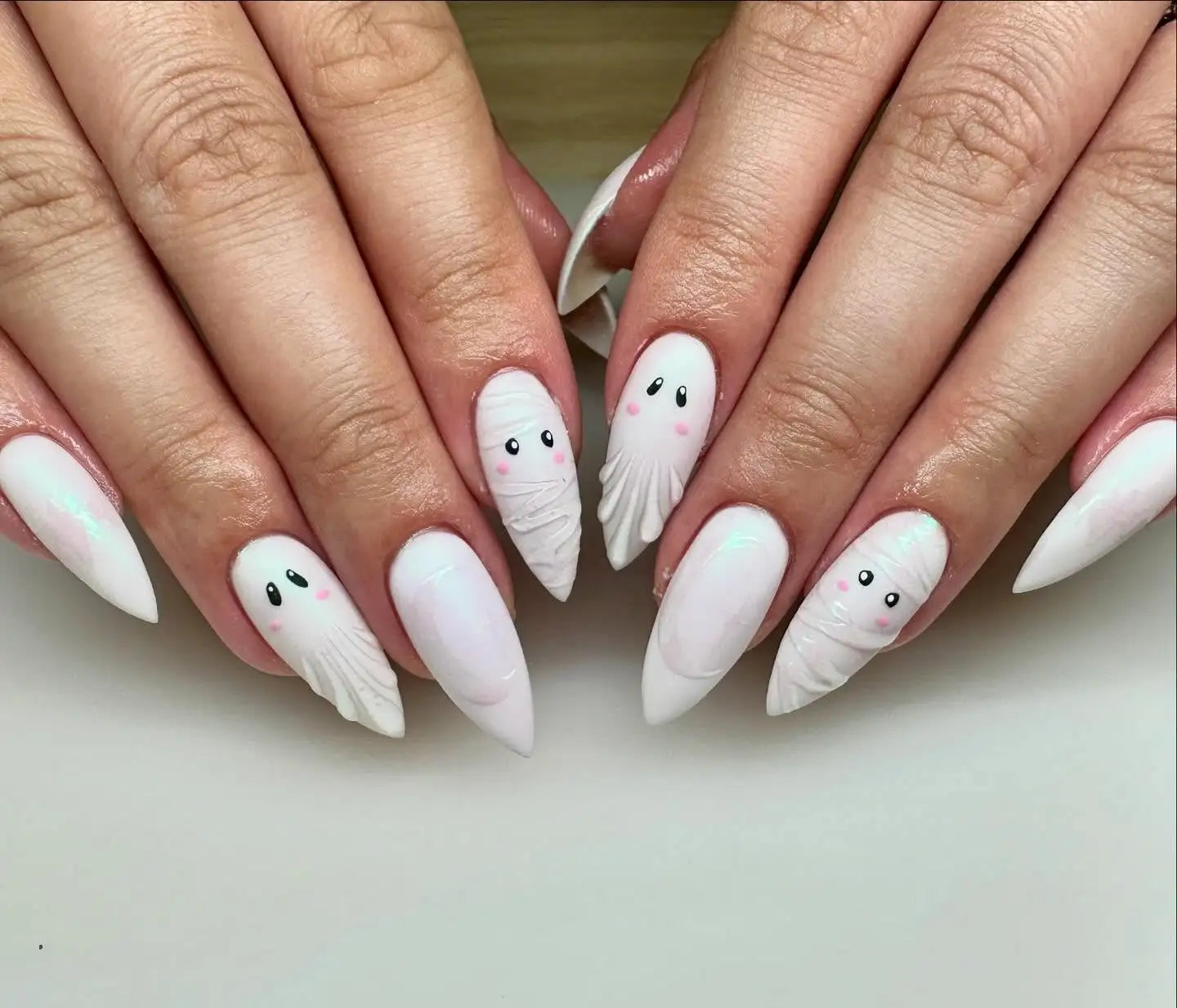 Hand with white stiletto press-on nails featuring cute ghost and mummy nail art designs.