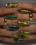 Hand with long press-on nails featuring gold, green, and teal abstract designs