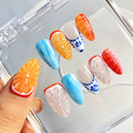 Handmade press-on nails with orange fruit designs, blue accents, and floral patterns in a case