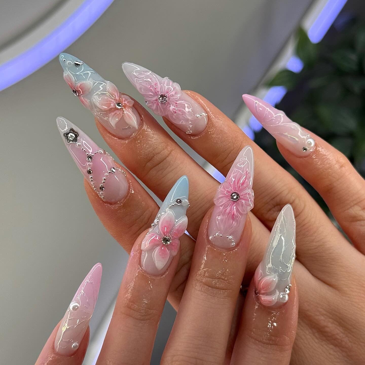 Hand with long stiletto press-on nails, pastel blue and pink, 3D floral and rhinestone design
