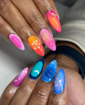 Hand with handmade press-on nails in vibrant pink, orange, and blue hibiscus floral designs