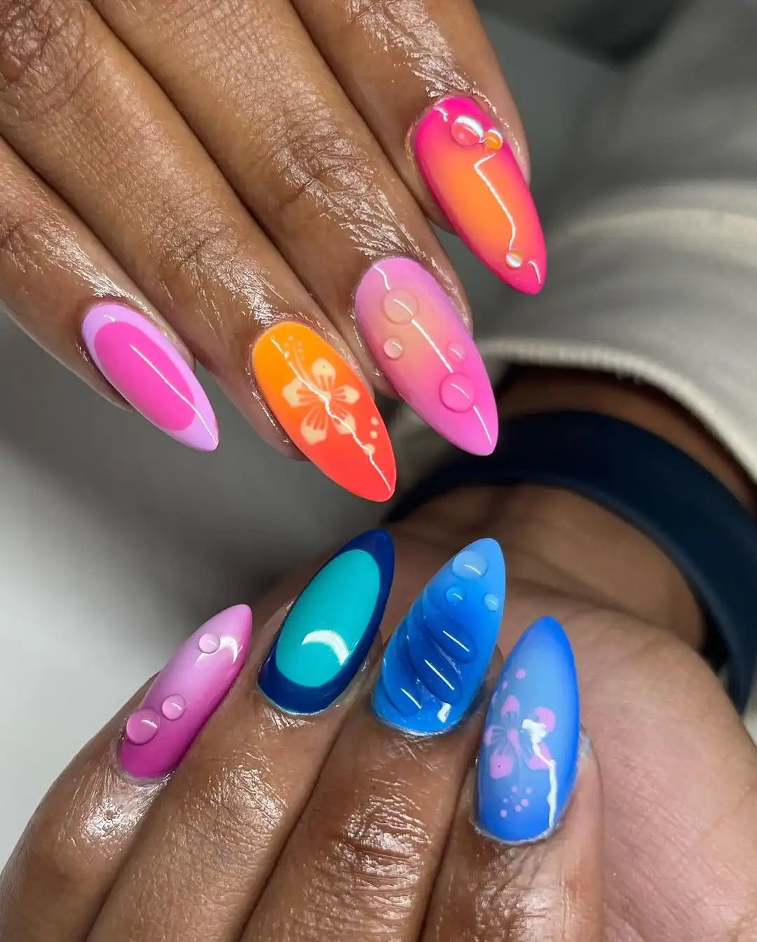 Hand with handmade press-on nails in vibrant pink, orange, and blue hibiscus floral designs