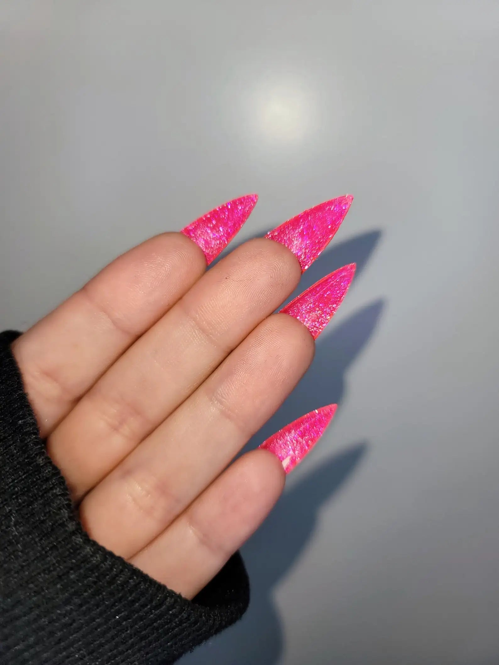 Hand with long stiletto-shaped pink glitter press-on nails, close-up
