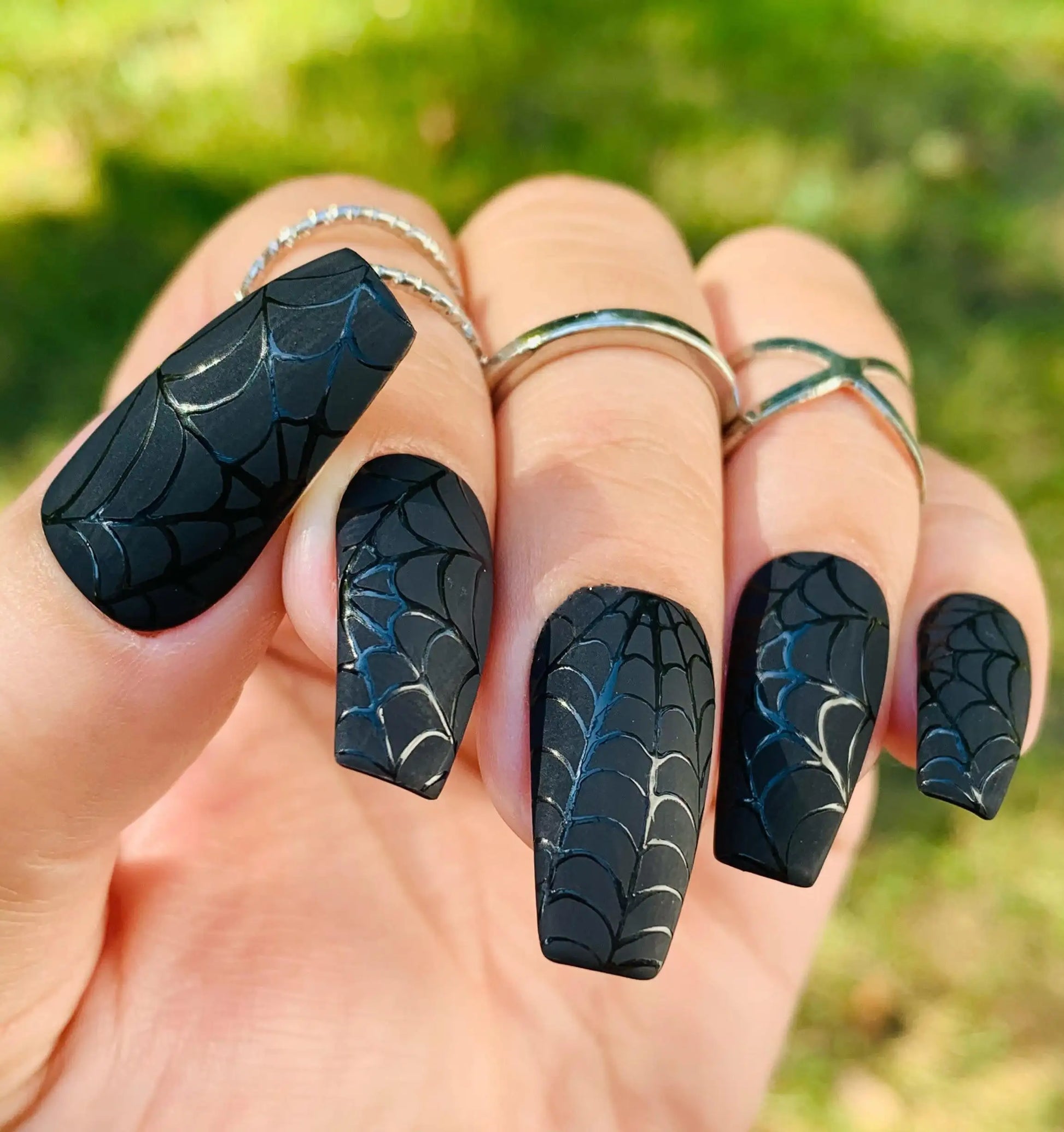 Hand with long black press-on nails featuring spider web designs, perfect for Halloween.