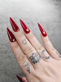 Hand with glossy red stiletto press-on nails and finger tattoos on a gray background