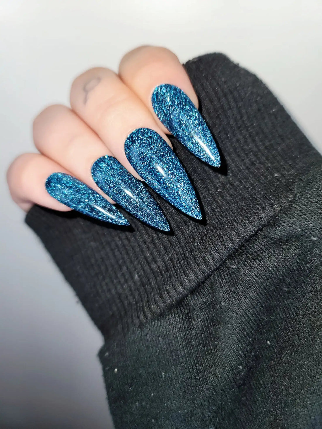 Hand with long blue glitter press-on nails in a stiletto shape