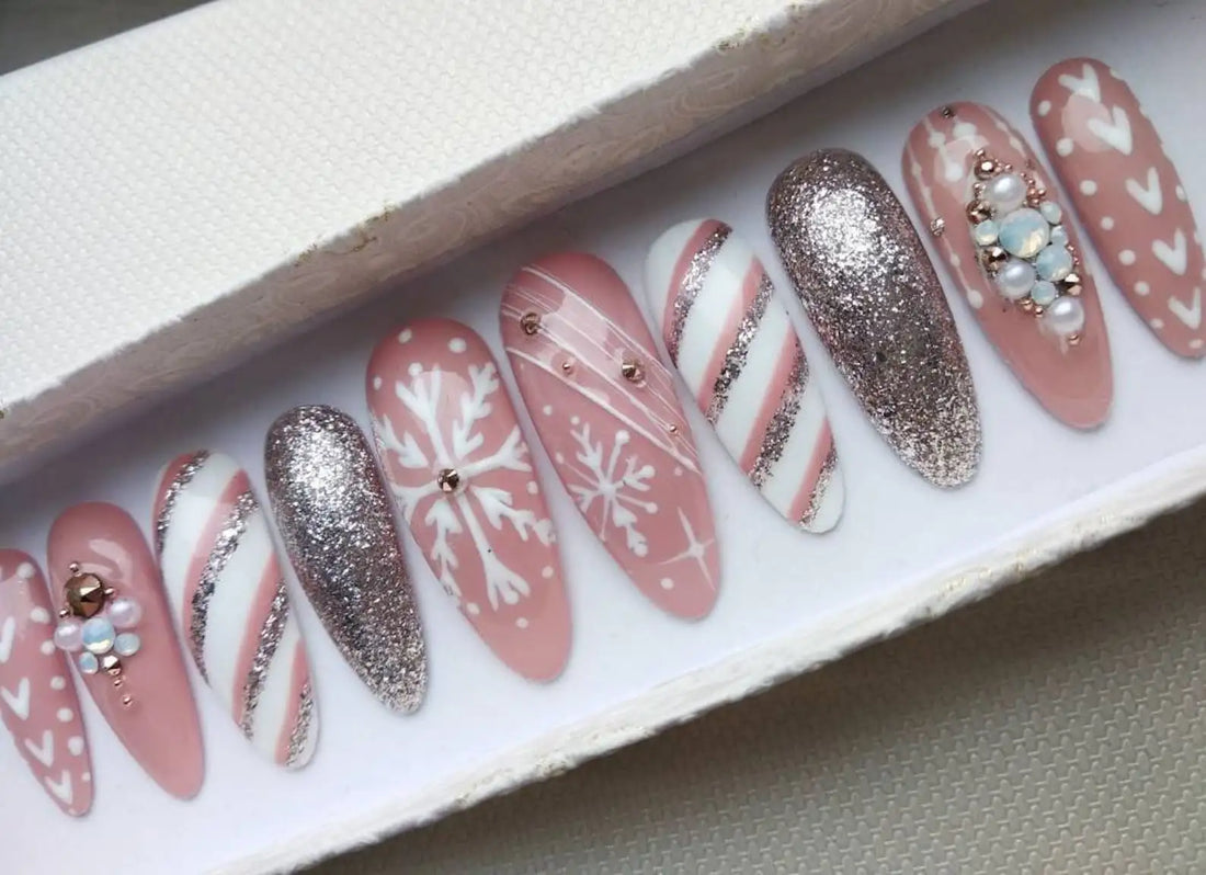 Pink press-on nails with white snowflake, glitter, candy cane, and pearl designs for Christmas.