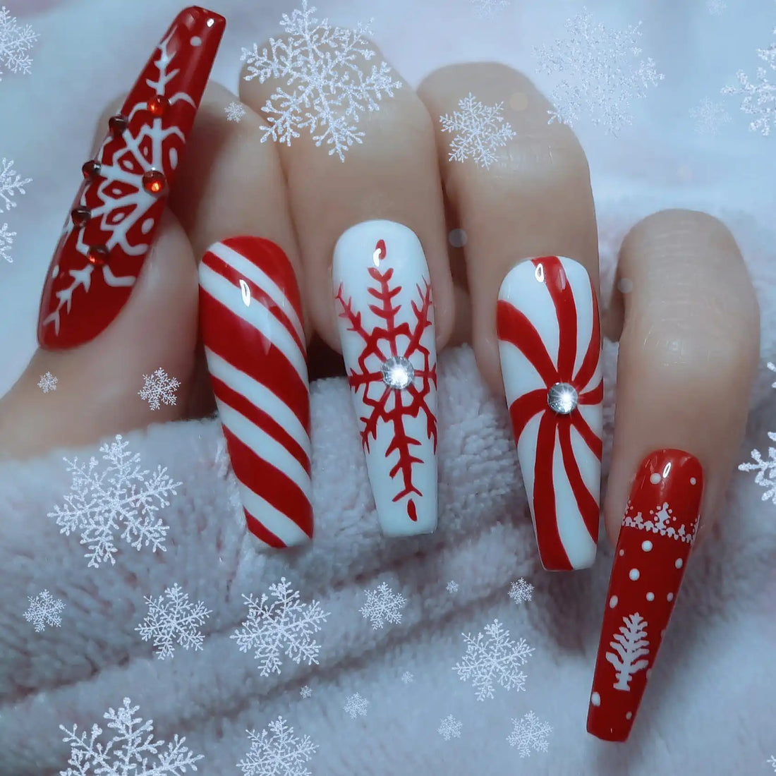 Hand with long press-on nails featuring red and white Christmas snowflake and candy cane designs.