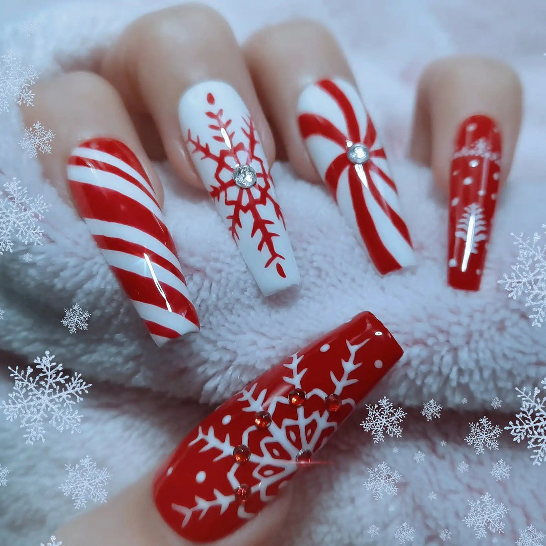 Hand with long press-on nails featuring red and white Christmas snowflake and candy cane designs.