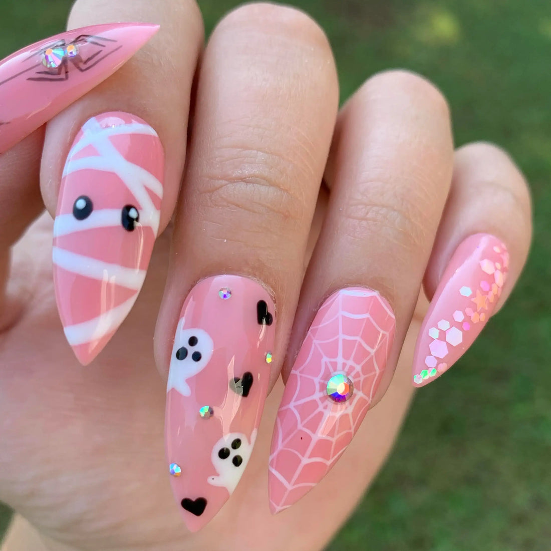 Pink Halloween press-on nails with ghost, spiderweb, mummy and glitter accents