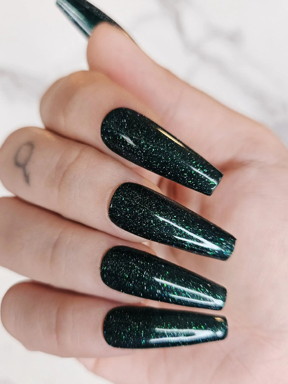 Hand with long dark green glitter glossy press-on nails, almond shape, close-up