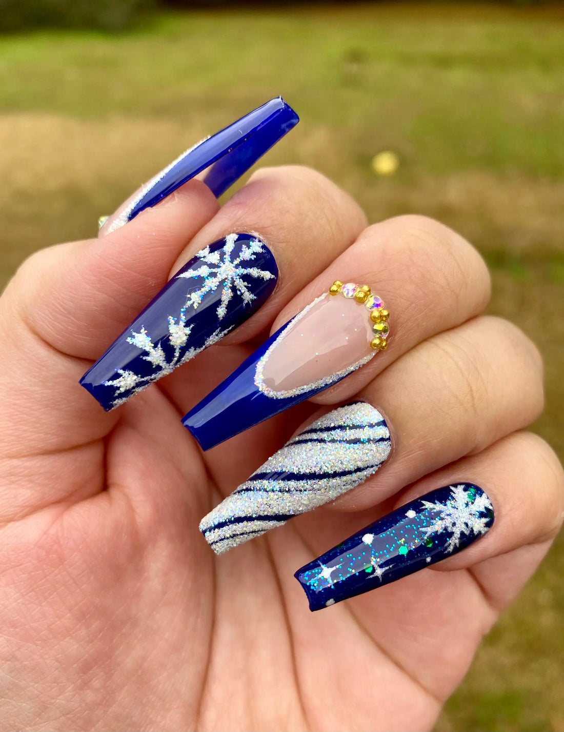 Long press-on nails with deep blue glitter, snowflake designs, silver accents, and gold gems