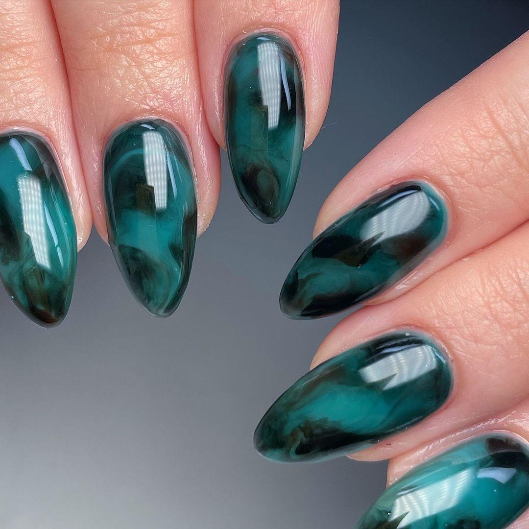 Almond-shaped deep green marble press-on nails with glossy finish on a hand