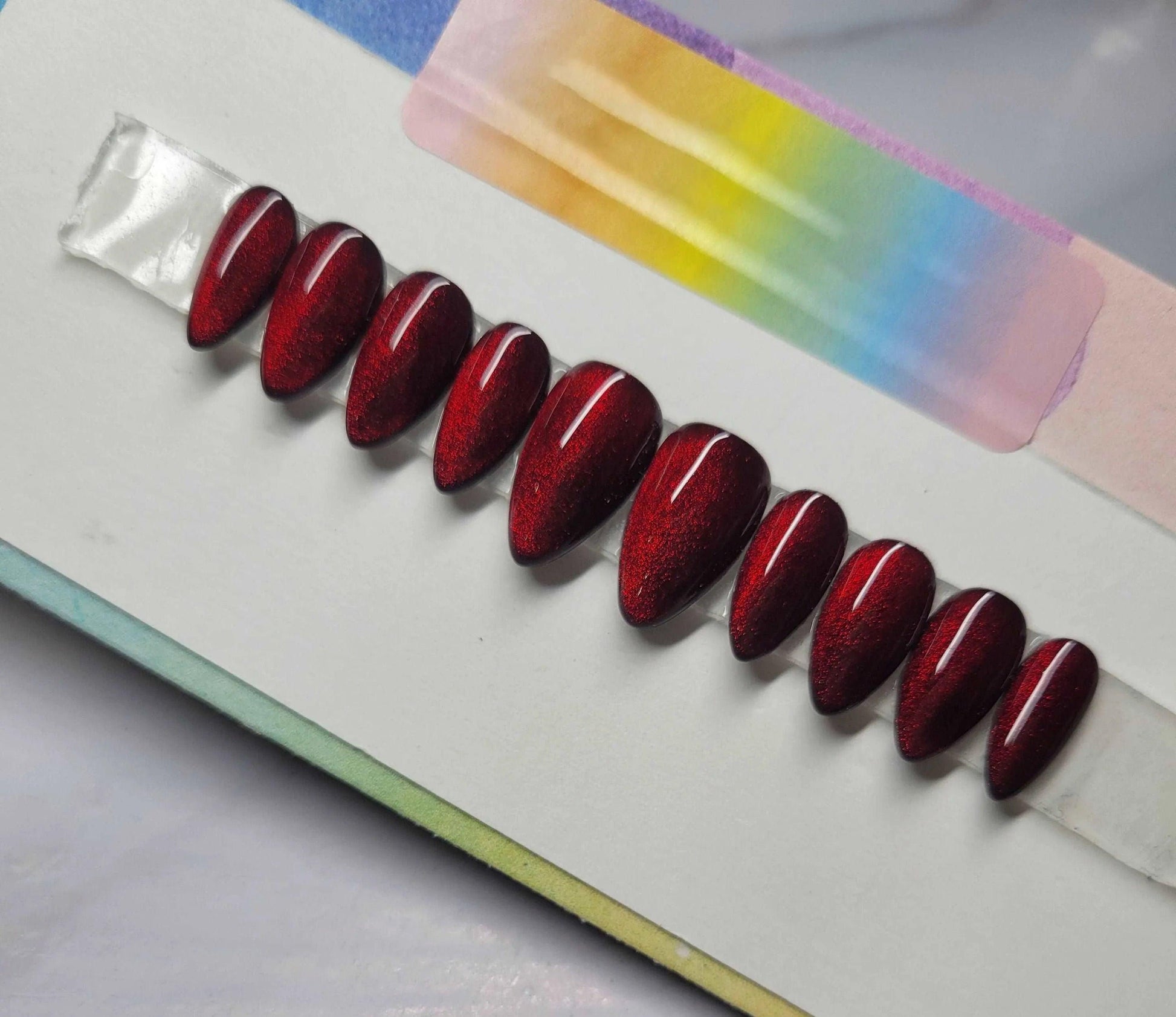 Custom red cat eye press-on nails with a glossy, shimmering garnet finish displayed in a row.