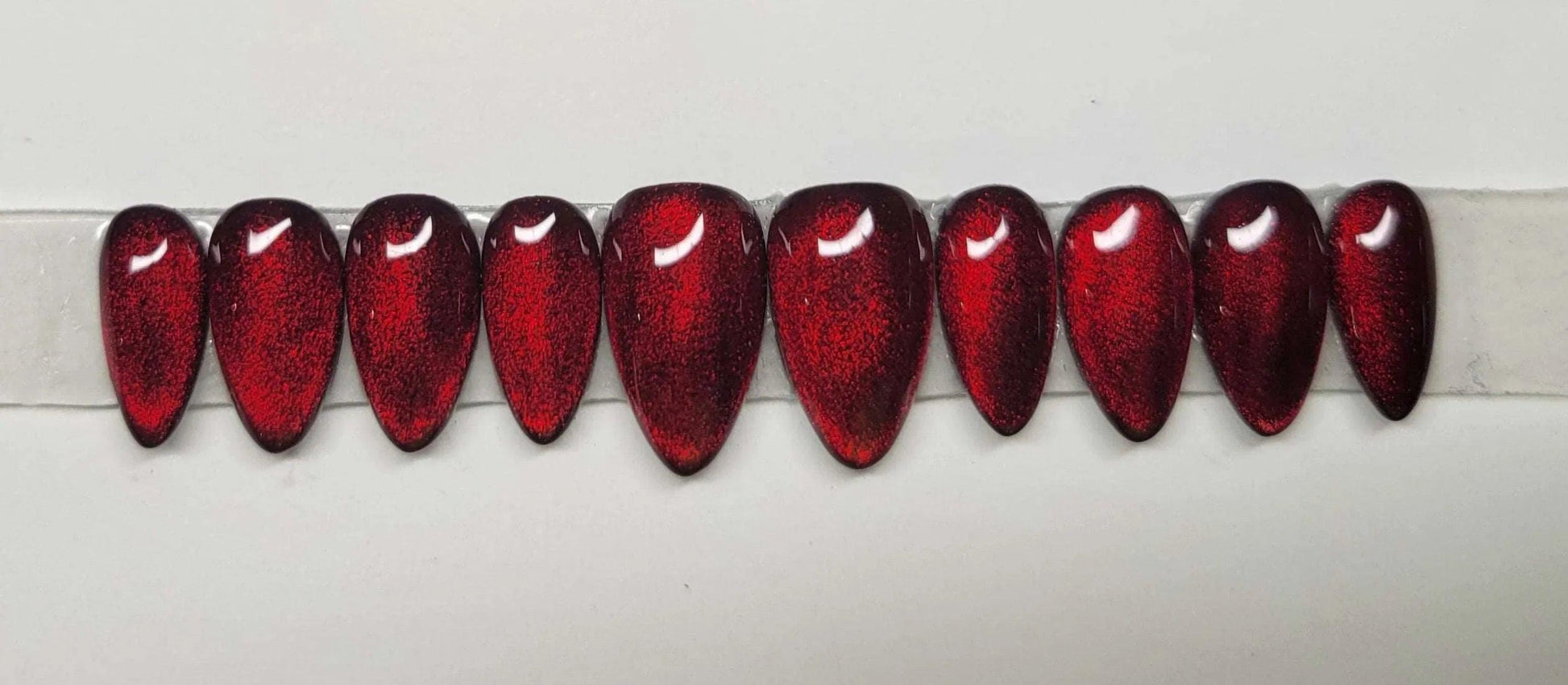 Set of glossy red cat eye stiletto press-on nails with a shimmer effect on white background