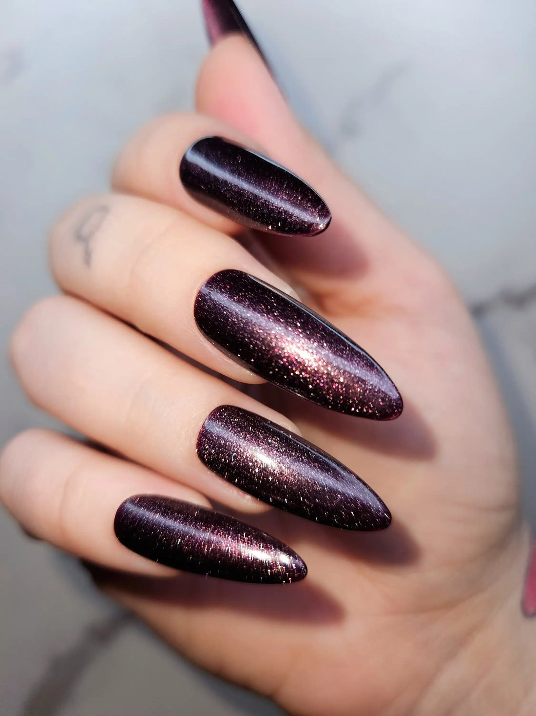 Hand with long almond-shaped dark glitter press-on nails, glossy and reusable design