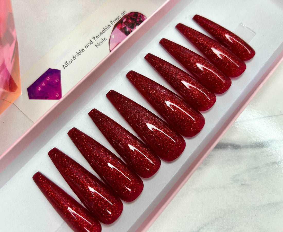 Coffin-shaped glittery red press-on nails in a pink box on a marble surface