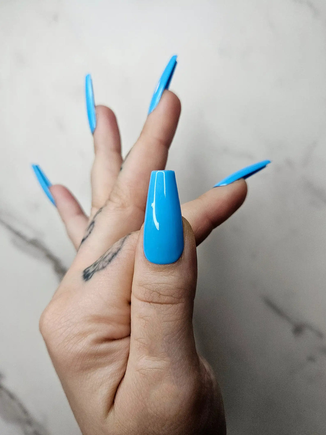 Hand with glossy blue coffin-shaped press-on nails against a light background