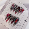 Red and black press-on nails with gothic silver cross charms and heart jewels