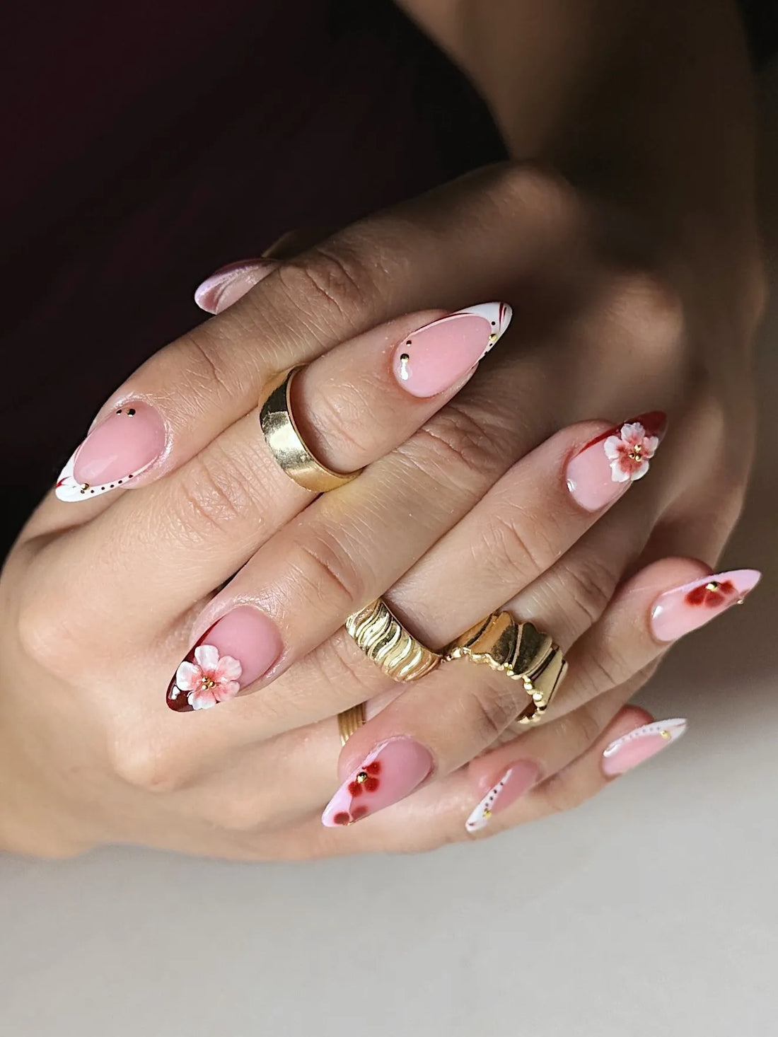 Hand with handmade 3D cherry blossom press-on nails, red floral French tips, gold beads.